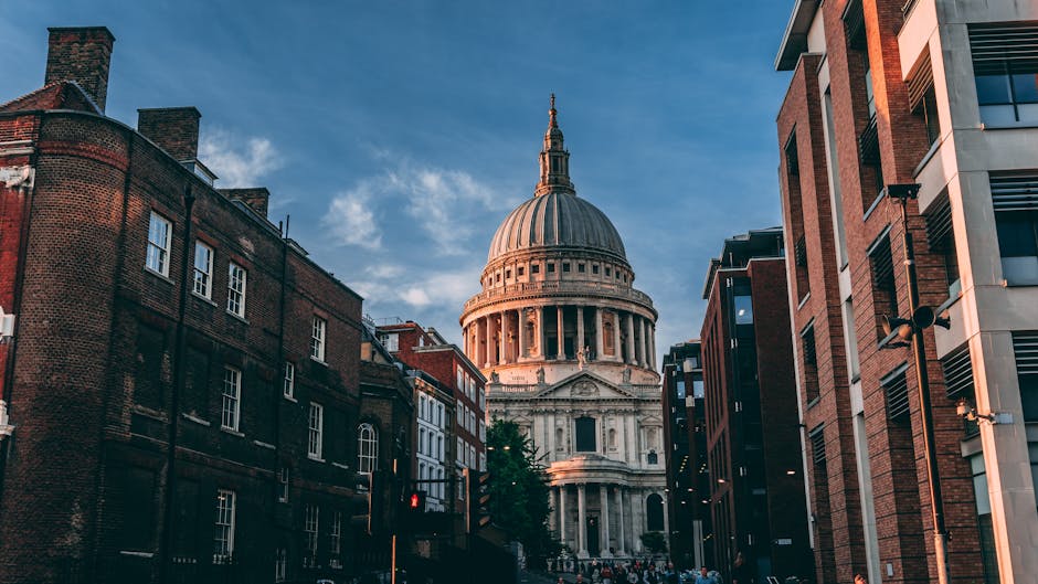 Photograph of a city street during daytime with St. Paul's Cathedral prominent in the background, featuring its large dome and classical architecture. The street is lined with a mix of older brick bui
