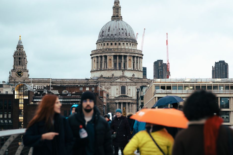 Photograph of a city street during daytime with St. Paul's Cathedral prominent in the background, featuring its large dome and classical architecture. The street is lined with a mix of older brick bui